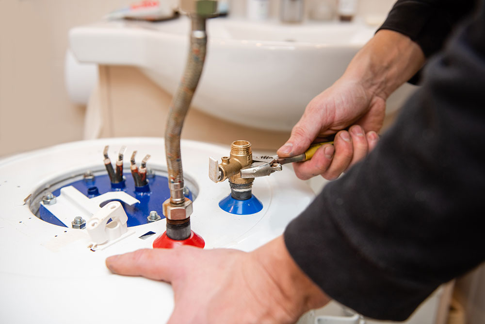 Technician repairing water heater with wrench, focusing on fittings and connections in a bathroom setting.