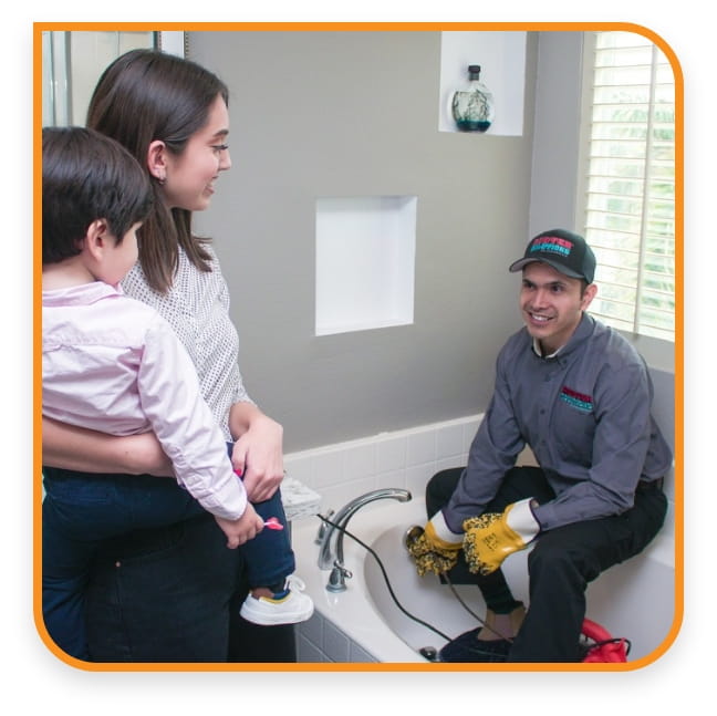 Professional plumber fixing bathtub while a mother and child watch, ensuring quality home service and customer satisfaction.