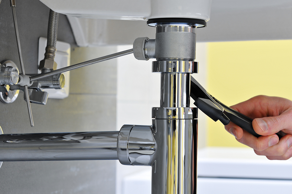 Hand using wrench to tighten plumbing under sink, showcasing a DIY plumbing repair.