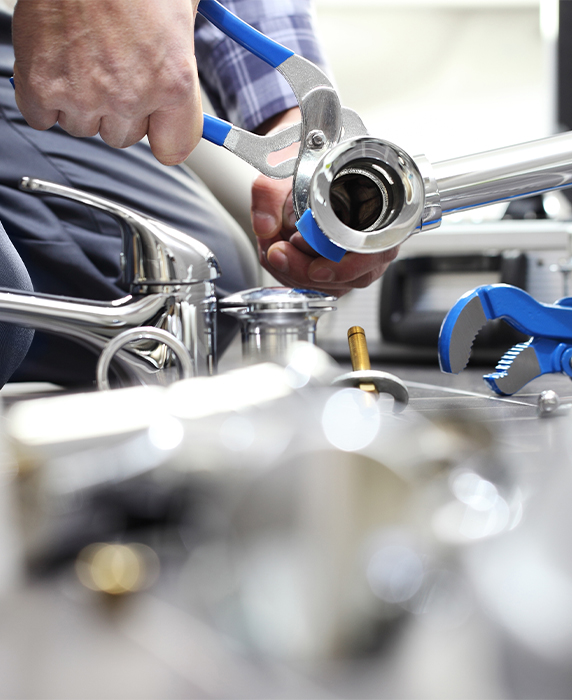 Plumber using a wrench to fix a pipe with various plumbing tools in the foreground.