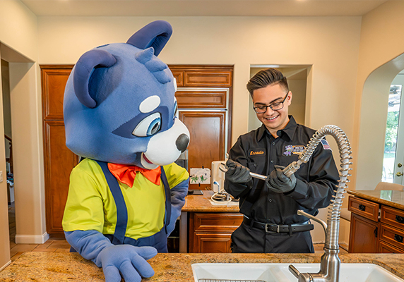 Cartoon mascot and technician fixing kitchen faucet in a bright home setting.