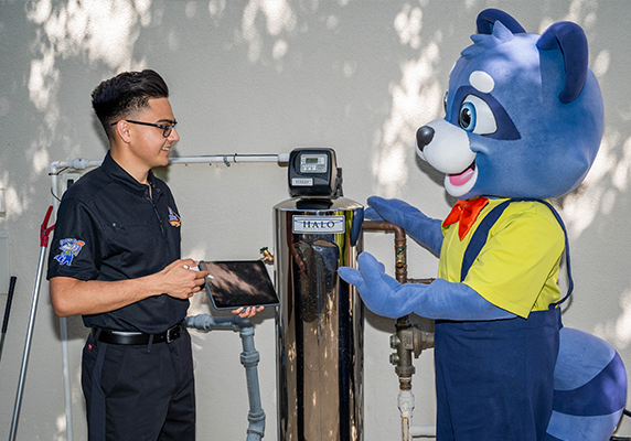 Technician and raccoon mascot discussing water softener installation outside.