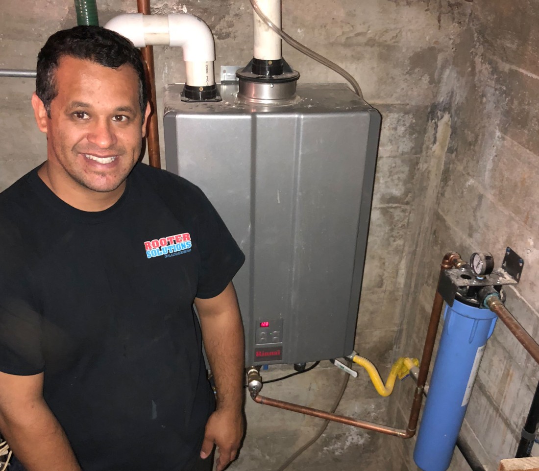 Man smiling near installed tankless water heater and filtration system in basement.