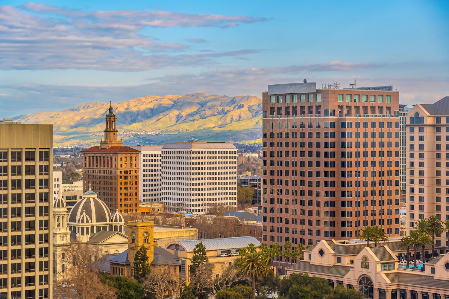 San Jose skyline with diverse architecture, mountain backdrop, under blue skies.