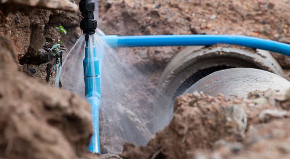 Leaking blue water pipe in a muddy trench indicates need for repair, highlighting infrastructure issues.