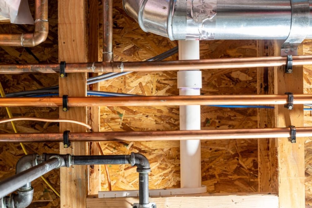 View of exposed copper plumbing and ducts in a wooden basement ceiling for home renovation or repair projects.