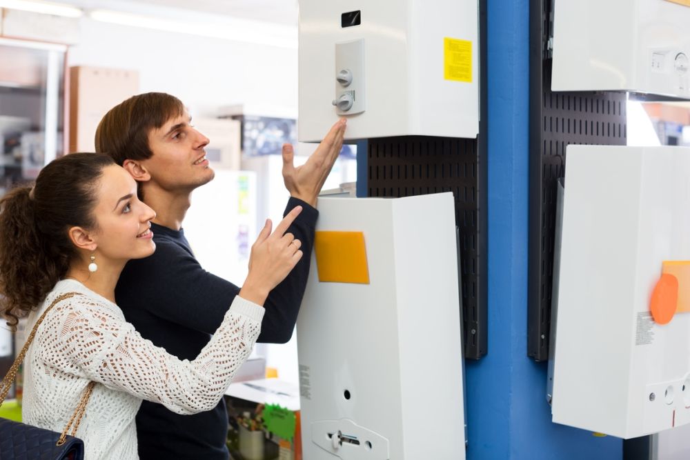 Couple shopping for a water heater in a store, examining models on display for home improvement needs.