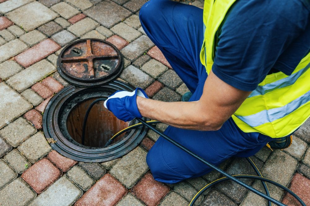 Worker cleaning sewer with cable on brick surface.