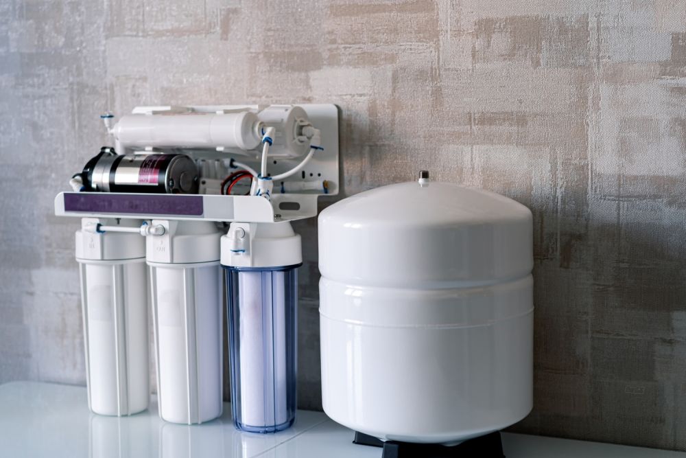 Reverse osmosis water filter system mounted on a wall, with storage tank, for home water purification.
