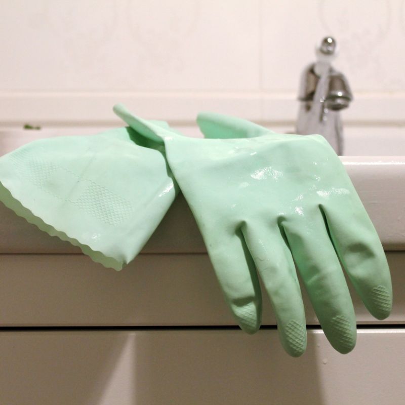 Mint green rubber gloves draped over a white bathroom sink, ideal for cleaning tasks.