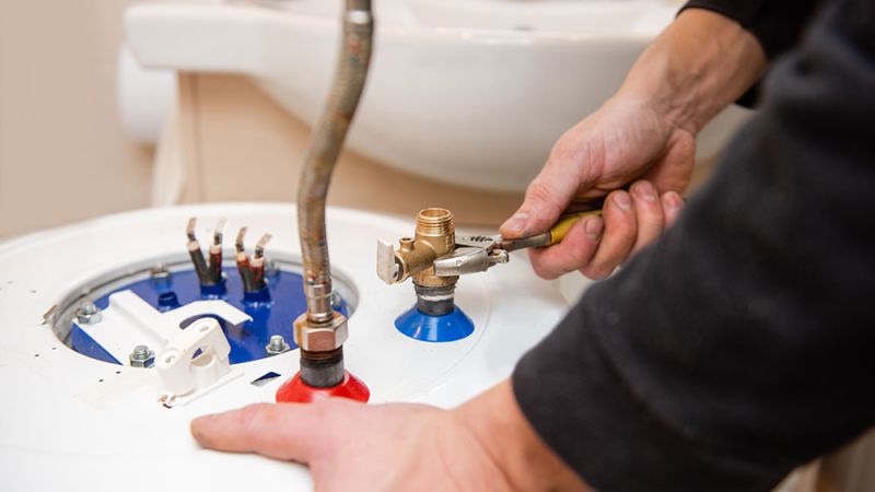 Technician repairing water heater with wrench, focusing on fittings and connections in a bathroom setting.