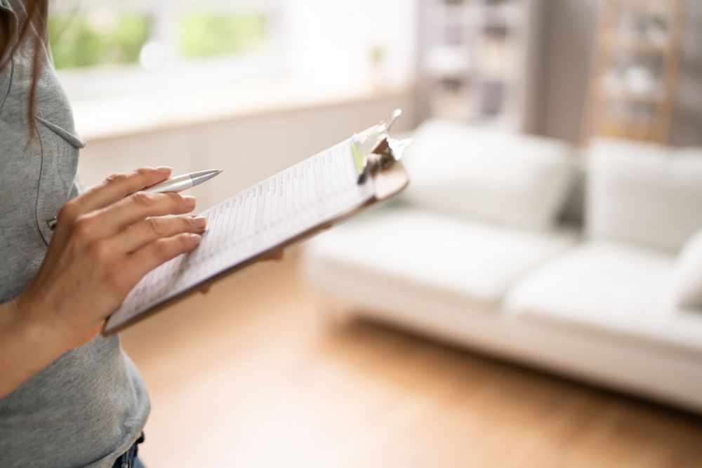 Person reviewing checklist on clipboard in bright living room setting.
