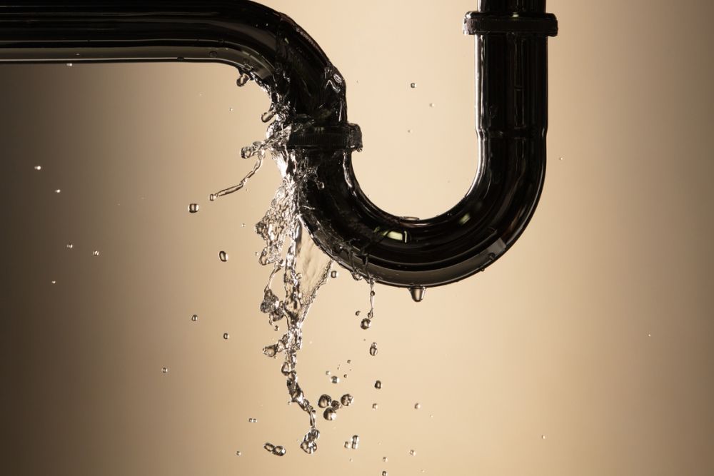 Leaking pipe with water flow, beige background, highlighting plumbing issues and repair needs.
