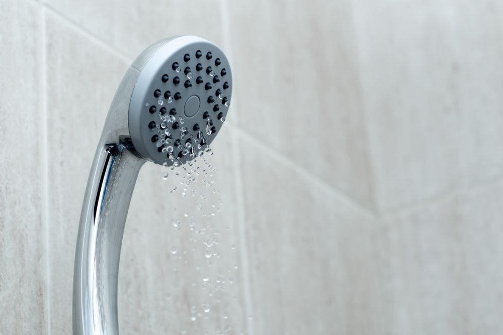 Modern chrome showerhead with water flowing in a tiled bathroom setting.