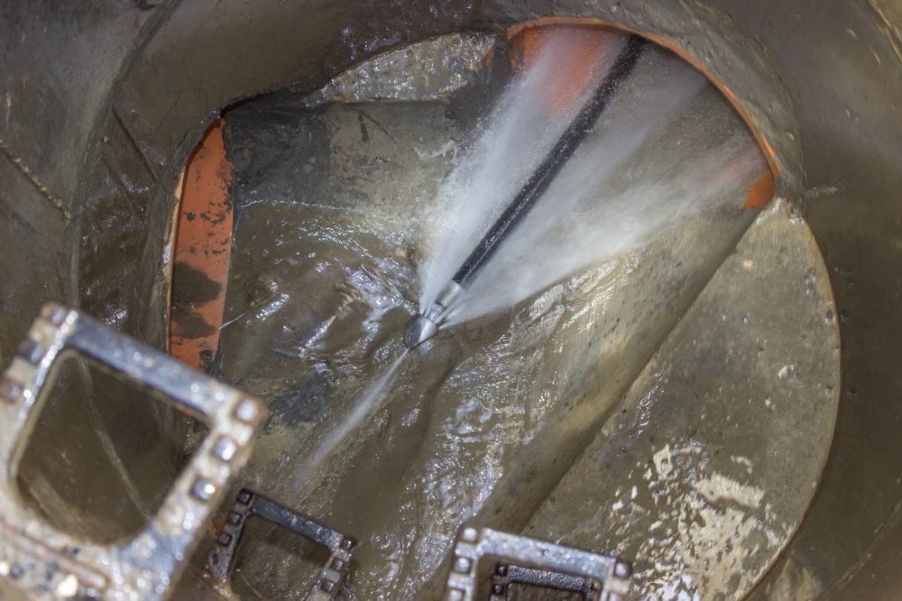High-pressure water jet cleaning a muddy sewer pipe interior.