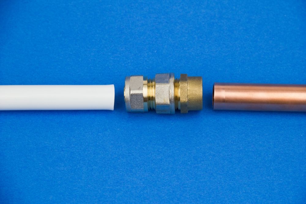 Plastic and copper pipes with a brass compression fitting on a blue background, illustrating plumbing connections.