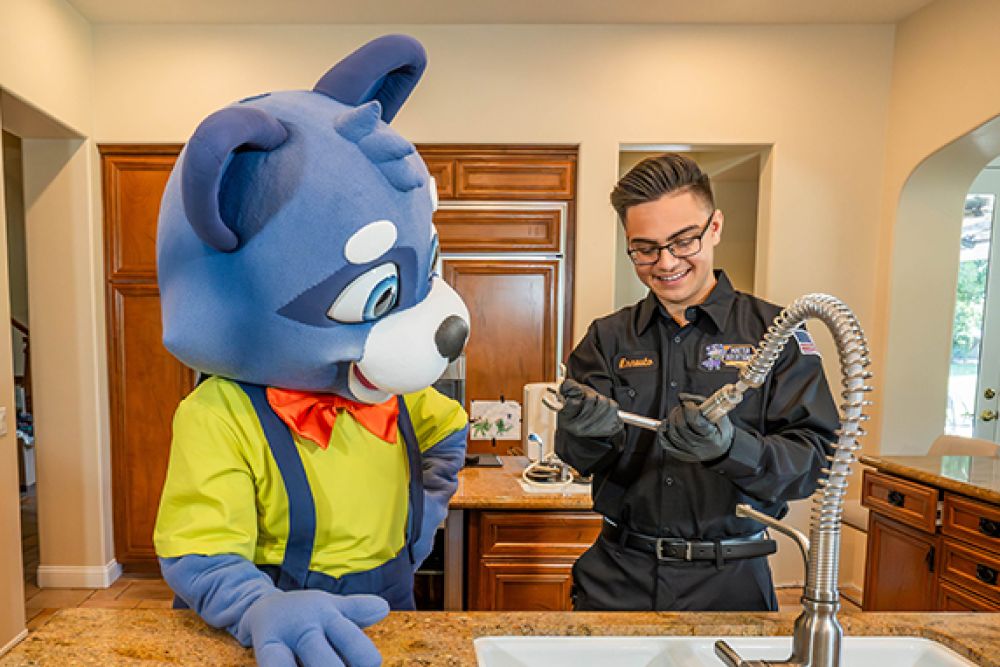 Cartoon mascot and technician fixing kitchen faucet in a bright home setting.