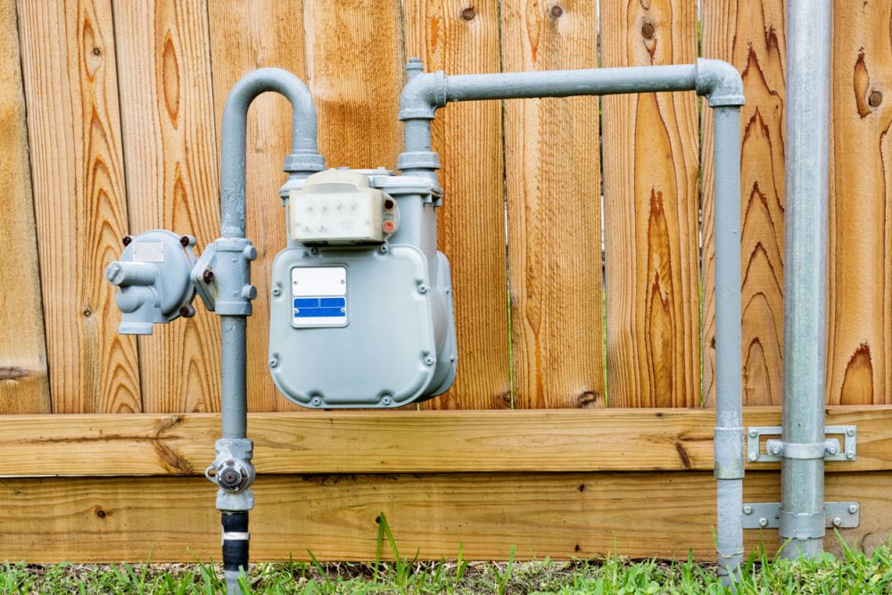 Outdoor residential gas meter with pipes against a wooden fence.