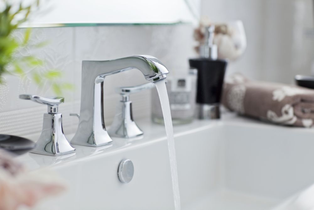 Modern bathroom faucet with running water in a stylish sink. Elegant decor with towels and dispensers.