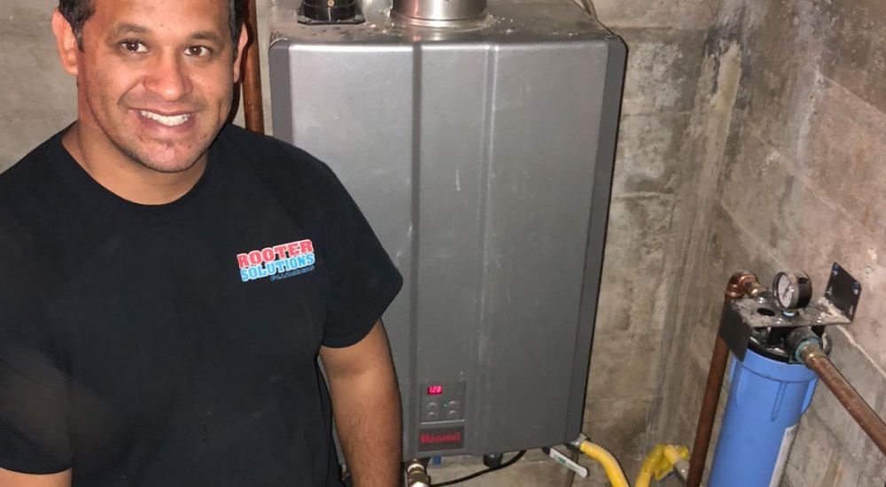 Man smiling near installed tankless water heater and filtration system in basement.
