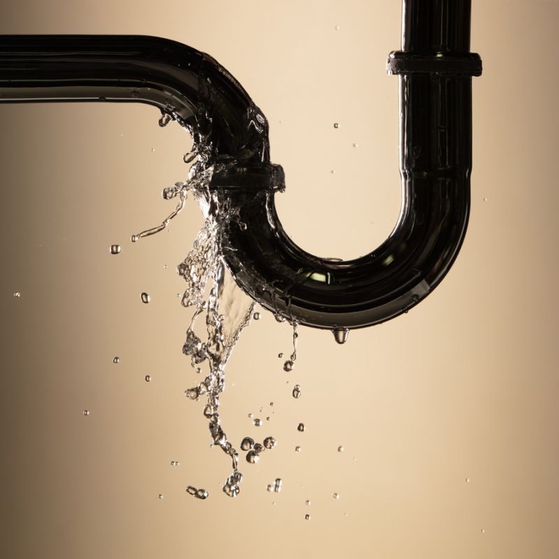 Leaking pipe with water flow, beige background, highlighting plumbing issues and repair needs.
