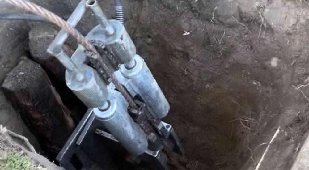 Hydraulic log splitter vertically positioned in a dug hole, showing the machine's mechanism and surrounding soil.