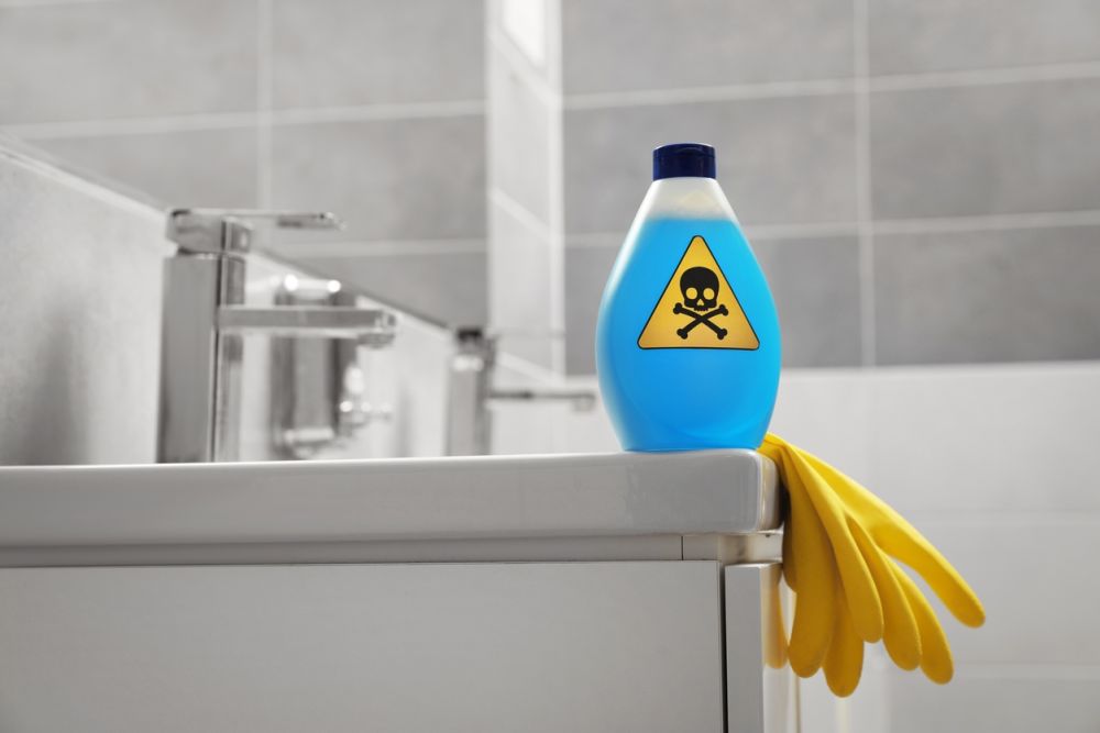 Bottle with hazardous symbol and cleaning gloves on bathroom sink, emphasizing chemical safety awareness.
