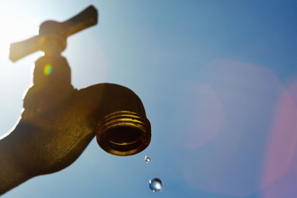 Close-up of a dripping brass faucet against a bright blue sky, highlighting water conservation and scarcity.