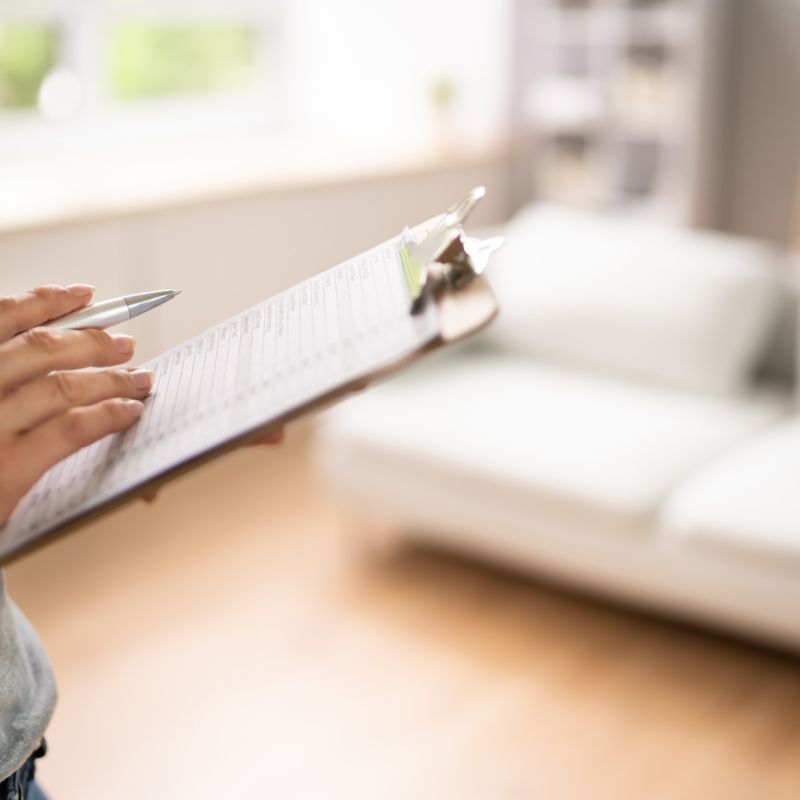 Person reviewing checklist on clipboard in bright living room setting.