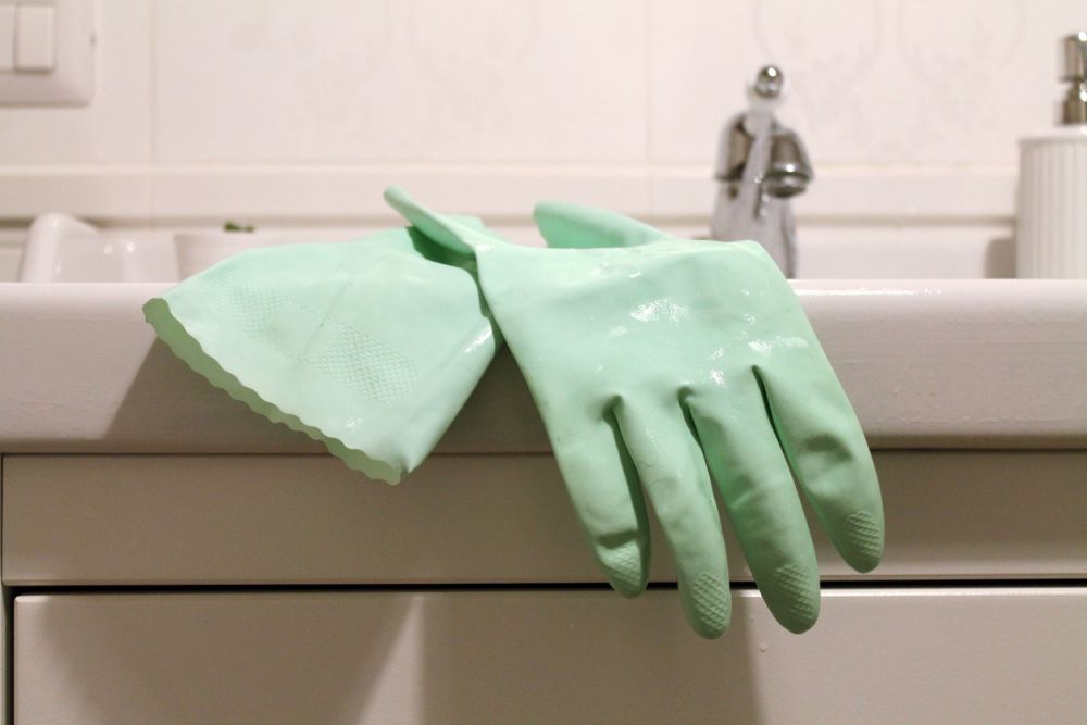 Mint green rubber gloves draped over a white bathroom sink, ideal for cleaning tasks.