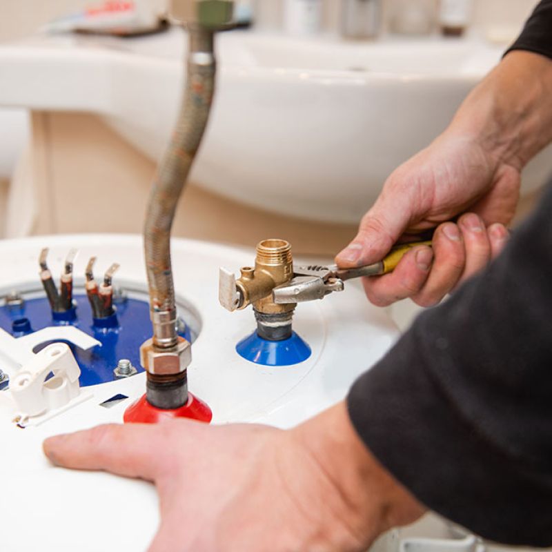 Technician repairing water heater with wrench, focusing on fittings and connections in a bathroom setting.