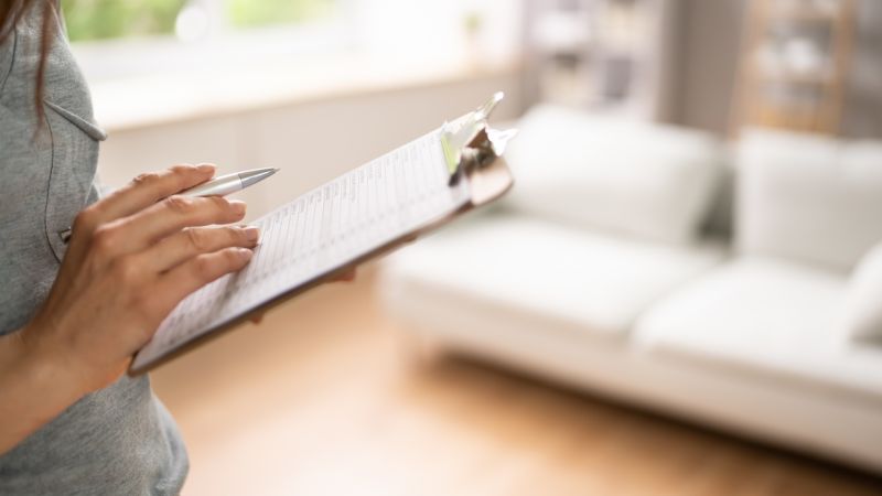 Person reviewing checklist on clipboard in bright living room setting.