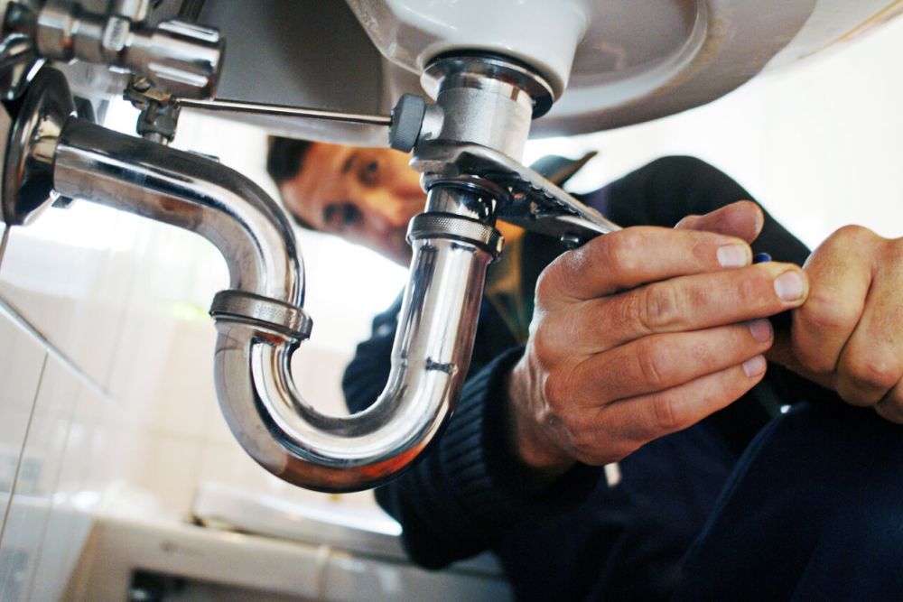 Plumber using a wrench to fix a sink pipe under a kitchen sink, ensuring efficient plumbing repair.