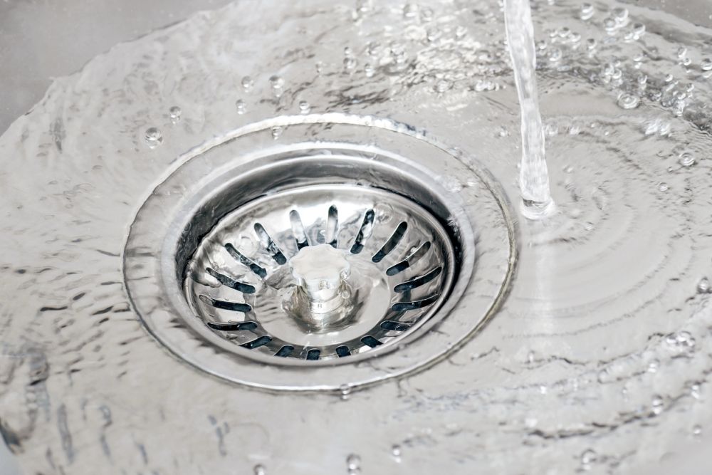 Water flowing down a stainless steel sink drain, creating ripples and bubbles on the surface.